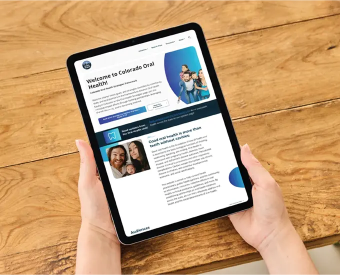 Hands holding a tablet showing a webpage above a wooden desktop.